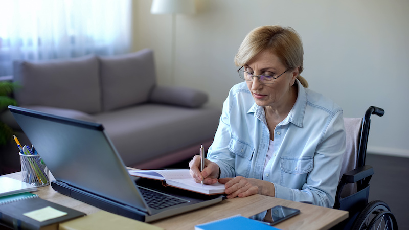 Handicapped grandmother making notes during online lesson home, senior student