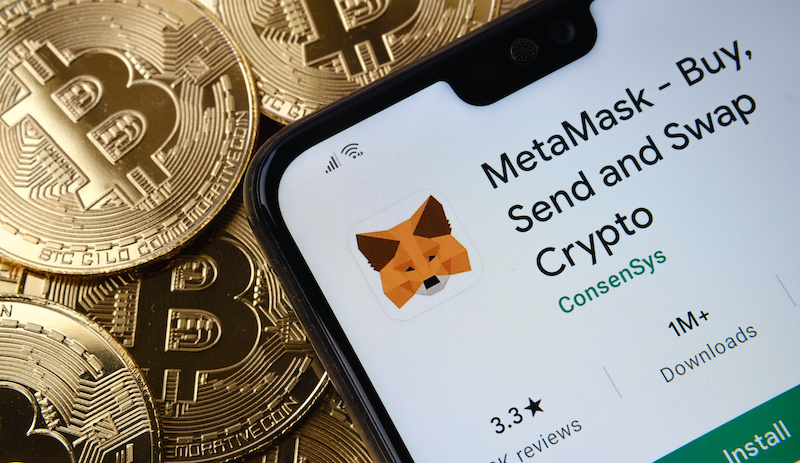 MetaMask app seen on the smartphone screen placed on top bitcoin coins pile.  
