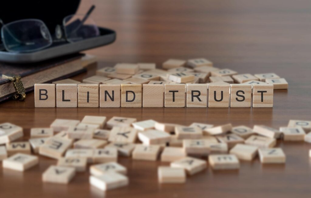 blind trust word or concept represented by wooden letter tiles on a wooden table with glasses and a book
