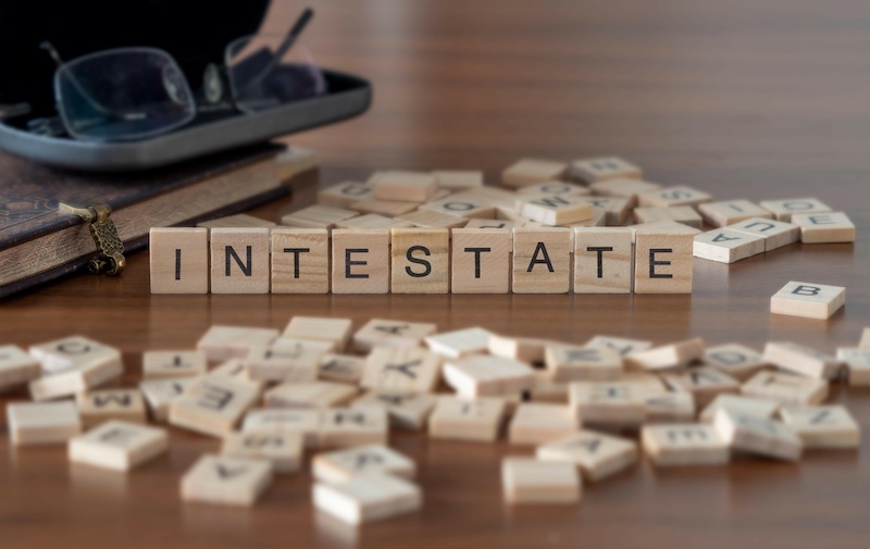 intestate word or concept represented by wooden letter tiles on a wooden table with glasses and a book
