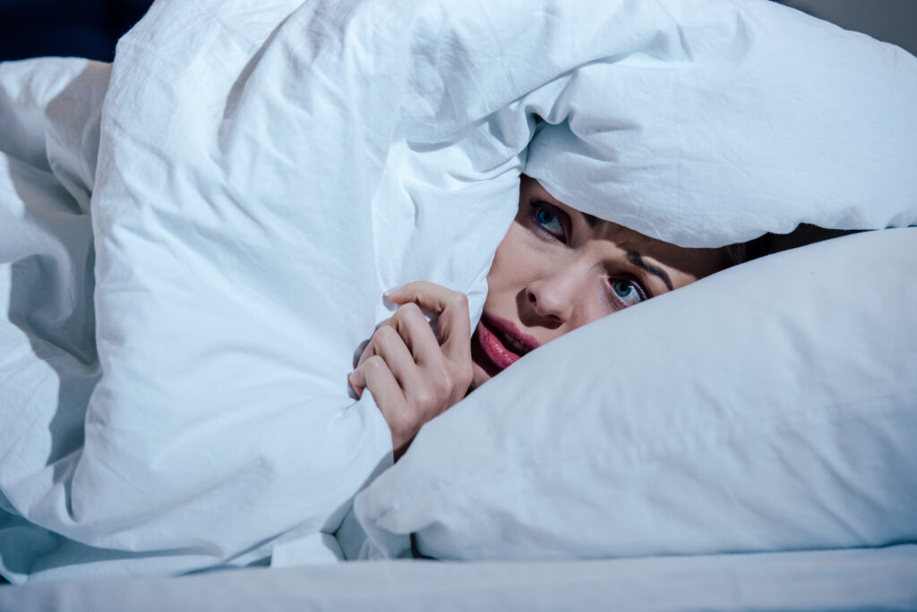 scared woman hiding behind blanket in bedroom at home