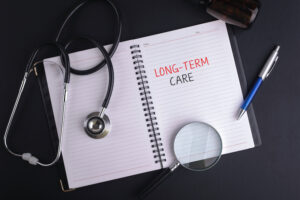 A note book with black ink pen written LONG-TERM CARE word, magnifying glass, bottle of pills and stethoscope on black table