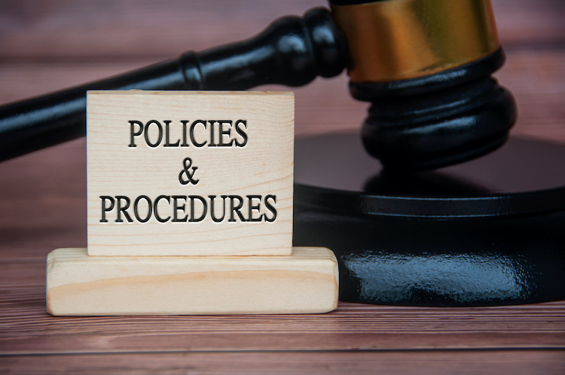 Policies and procedures text engraved on wooden block with gavel background. Policy and procedure concept.