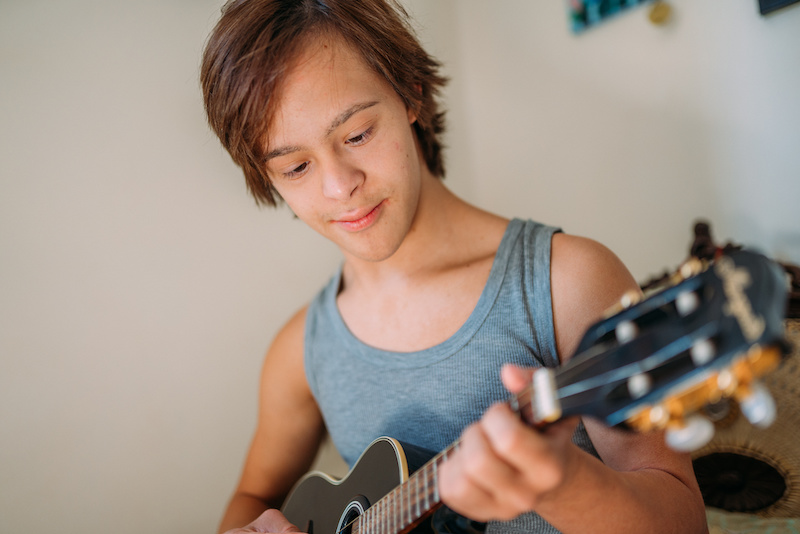 Cheerful Latin disabled boy with Down syndrome playing ukulele.