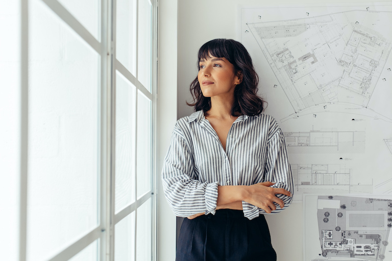 Confident female architect standing in office. Portrait of businesswoman standing with arms crossed and looking away.