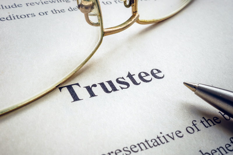 Glasses and pen on trust with word "trustee" featured