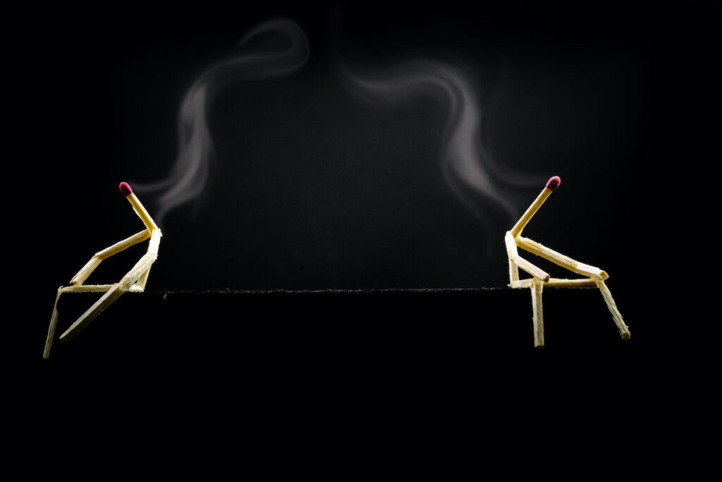 Concept of estrangement or discussion of couple, conflict relationship. Two characters made of matchsticks sad and sitting in the dark, one away from the other.