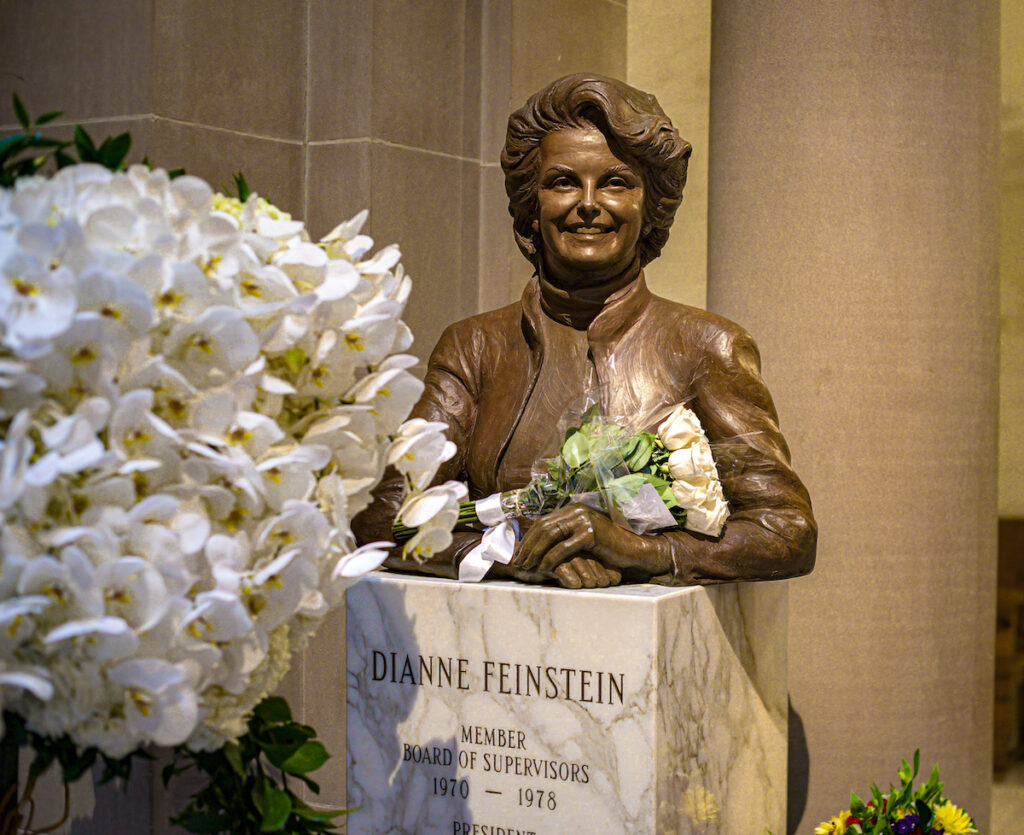A photo of the bronze bust of Senator and former San Francisco mayor Diane Feinstein, with flowers, during her public lying in-state at San Francisco City Hall.