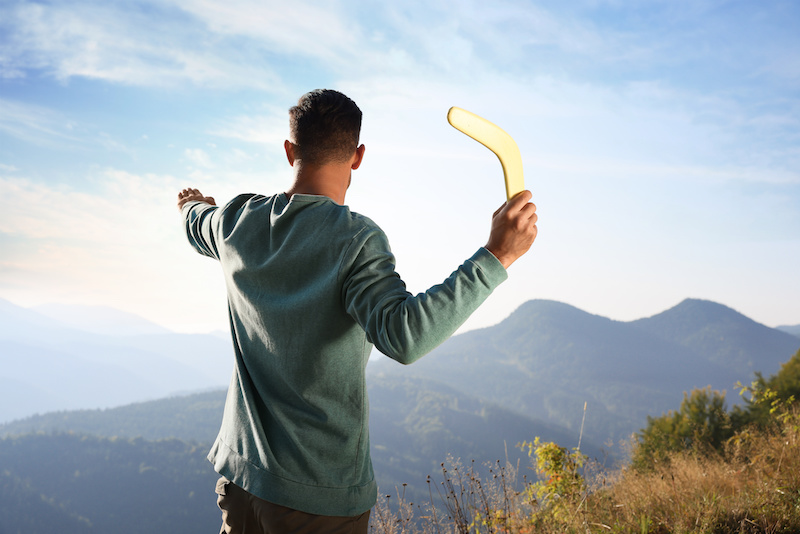 Man throwing boomerang in mountains on sunny day, back view