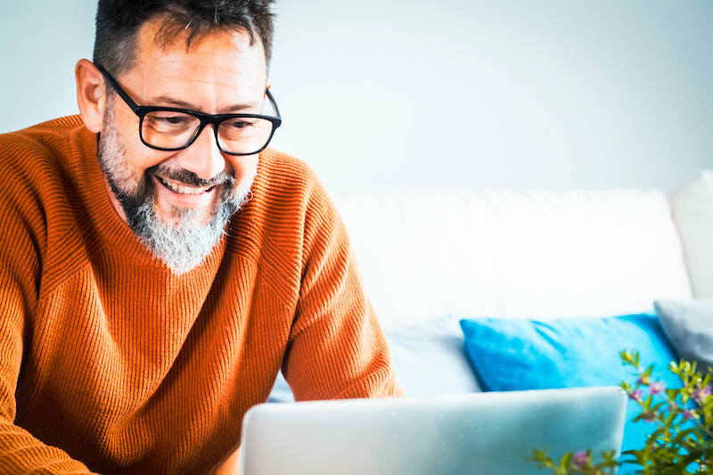 Smiling senior 50s man sit relax on sofa in living room browsing internet on modern computer gadget, happy mature freelance worker rest on couch at home watch video surf wireless web on. Searching web