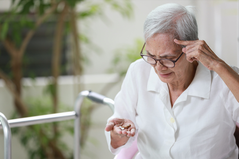 Asian senior patient with Alzheimer's disease or dementia,look at the pills capsules on her palm,trying to think,confused,old elderly people forget to take the medication,fail to remember or amnesia