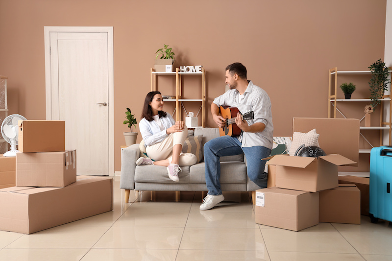 Happy young woman with her husband playing guitar in room on moving day