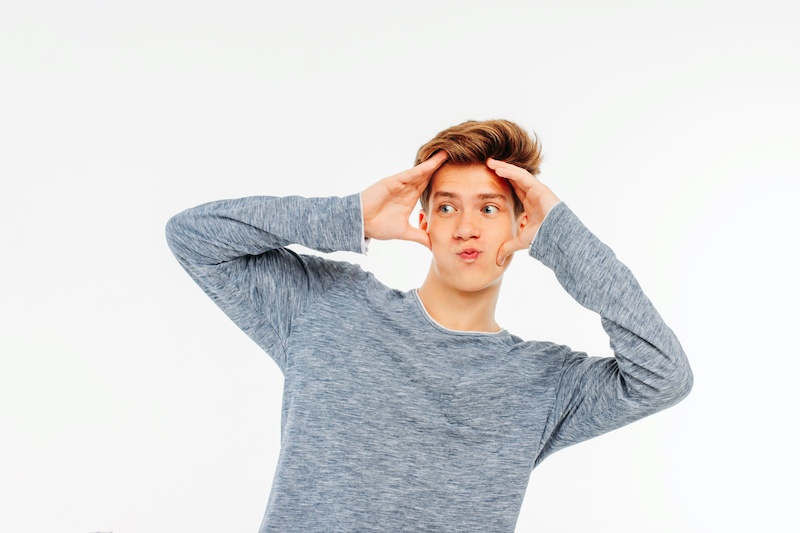 Young guy teenager is surprised, hands behind his head and looks away on white background