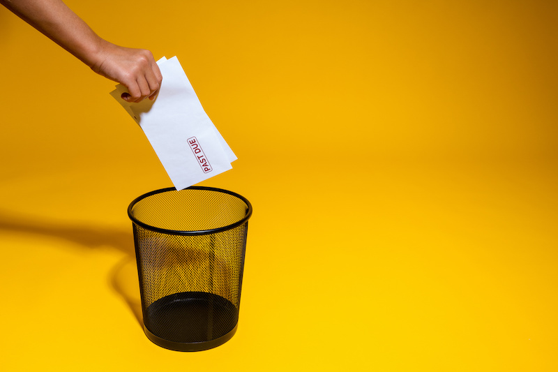 The hand throws into the trash envelopes with a bank red mark overdue. Postal envelopes are thrown into the wastebasket. Paper mail creates waste and pollutes the environment.