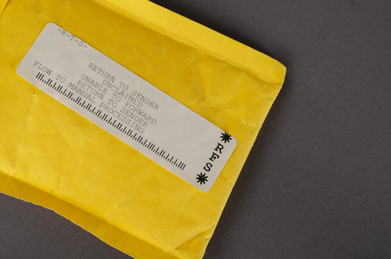 A yellow mail bag that says RETURN TO SENDER. Undelivered package on a gray background. Top view, no people.