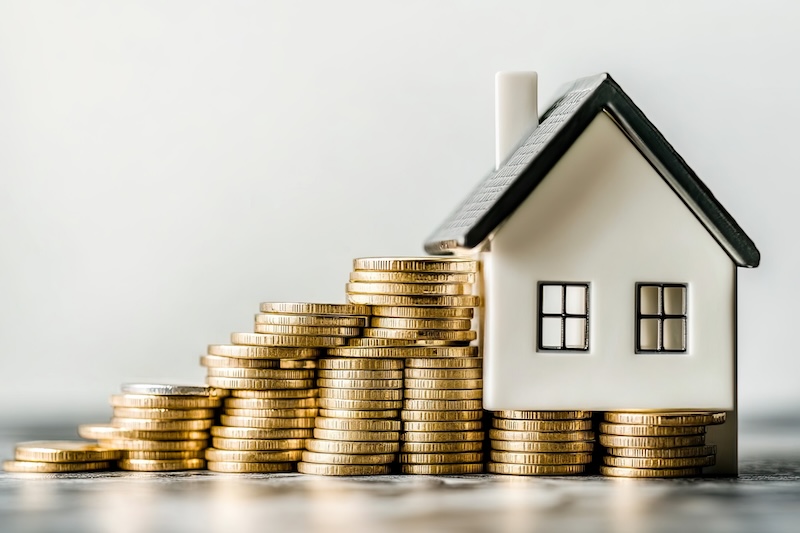 A small house model next to stacks of coins, symbolizing real estate investment and finance.