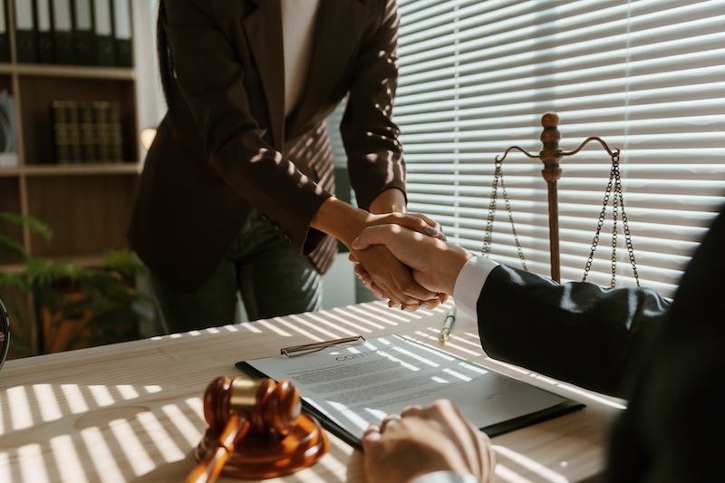 Lawyers shaking hands after signing a contract with a gavel and scales of justice in the foreground