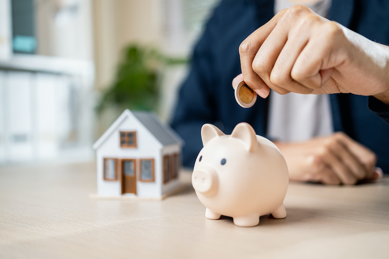 A person saving money with piggy bank and house model