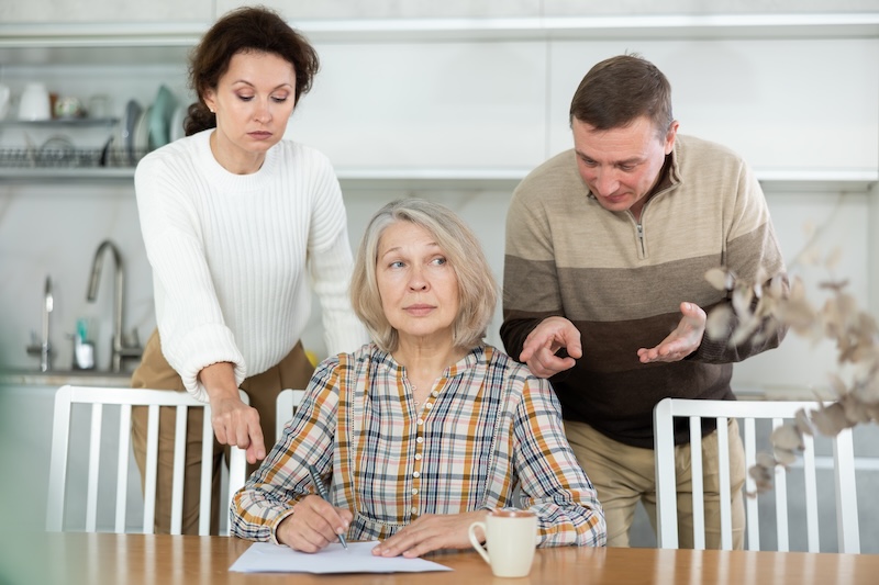 Middle-aged family members partitioning inheritance with mother sitting at kitchen-table with a sheet of paper and pen in hand