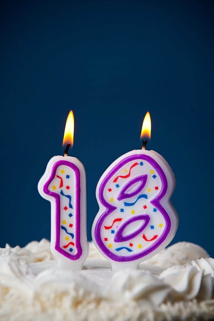 White iced cake on blue background with candles to celebrate various birthdays.