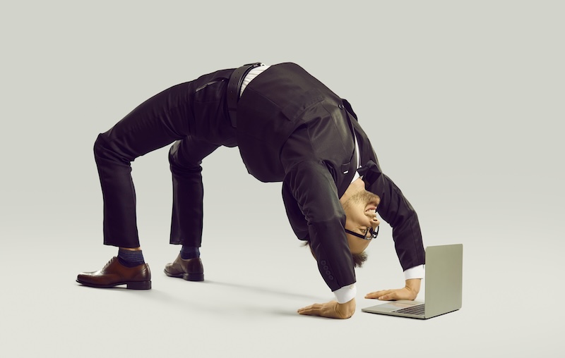Happy energetic businessman practises yoga positions while working on laptop computer. Funny fit flexible young man in suit and glasses doing bridge pose on studio floor while using modern notebook PC flexible child's trust