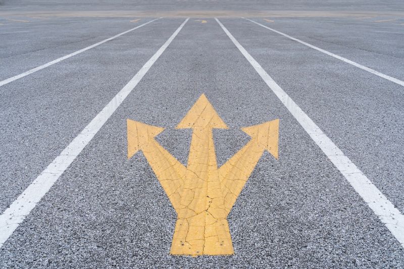 Painted and weathered yellow arrows on a street in Funchal. Disruptive ideas in business with three-way direction arrow sign, signifying creativity and differentiation in competitive environments.