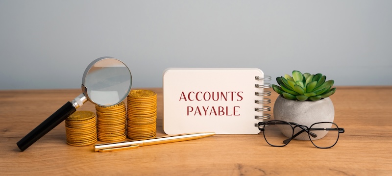Accounts payable concept. Amount of money a company owes to its suppliers or creditors for goods and services received but not yet paid for. Notebook with inscription, stacks of coin, magnifying glass