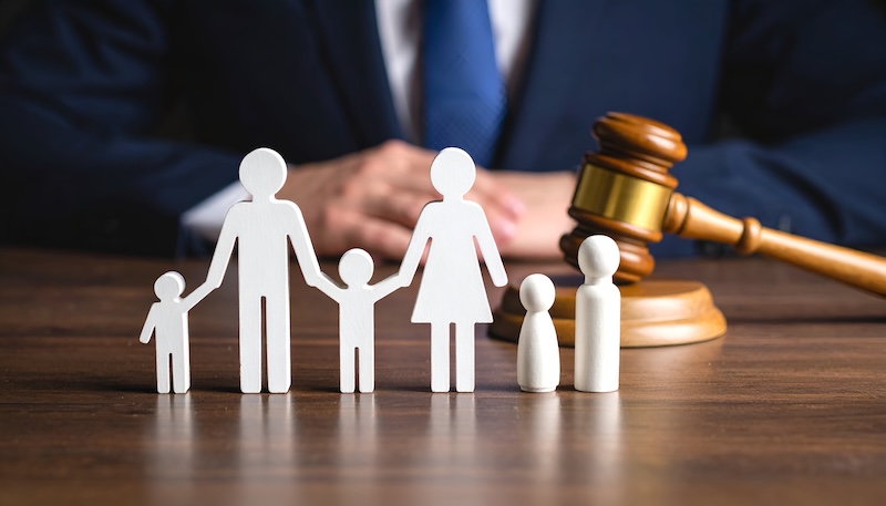 White paper family figures sit before a judge's gavel on a wooden table, symbolizing family law and legal proceedings.