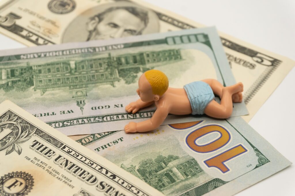 Miniature baby toys on the table with dollar bills. A metaphor for the monetary cost of parenting. investment in education. family expense.childcare costs