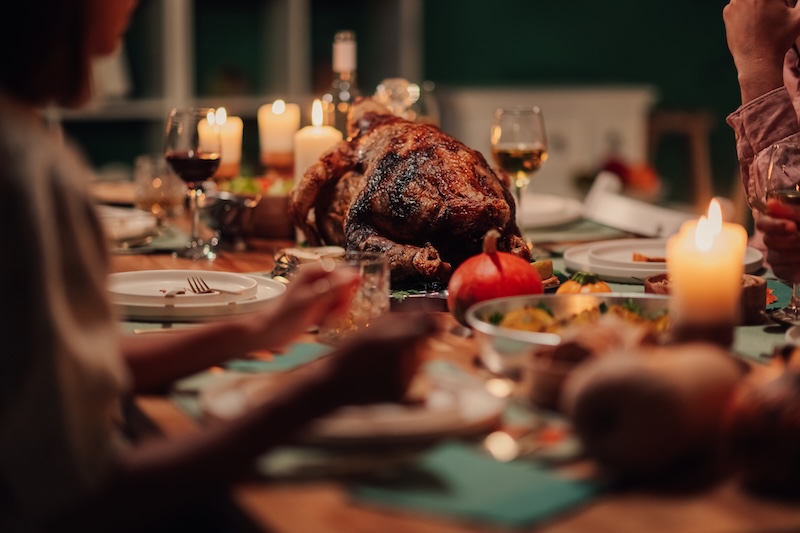 Family members are gathering around a thanksgiving table, enjoying a roasted turkey dinner with candles and autumn decorations