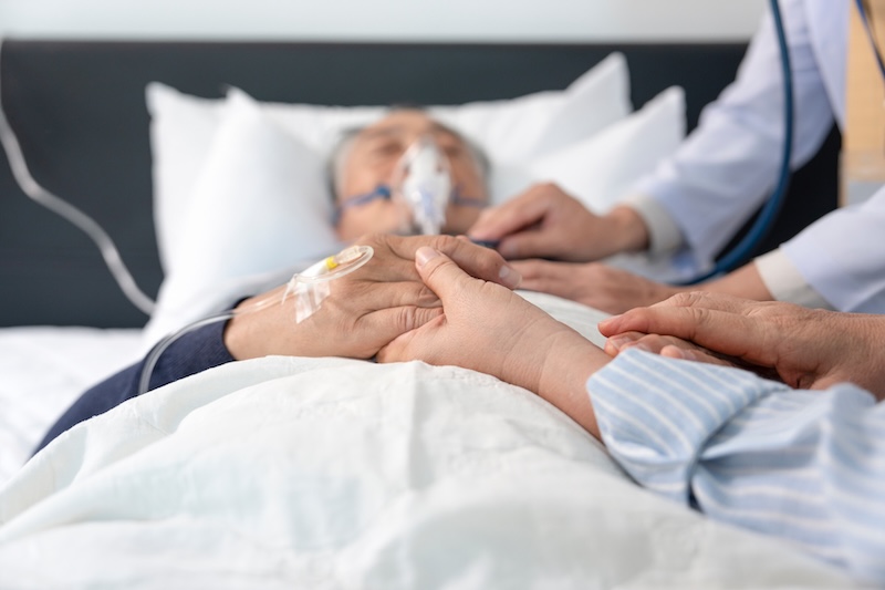 scene of a wife holding hands hopeless senior male patient who have oxygen and intravascular solution drip lying on bed,doctor examining a dying patient,concept of palliative care,end of life care