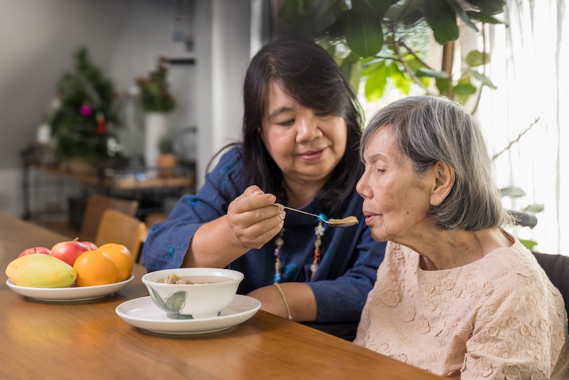 Daughter feeding elderly mother with soup fiduciary caregivers