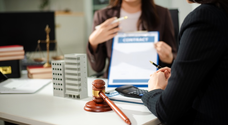 Real estate lawyer reviewing property contract with building model and gavel, concept of investment agreement, mortgage consultation, legal compliance and business transaction.