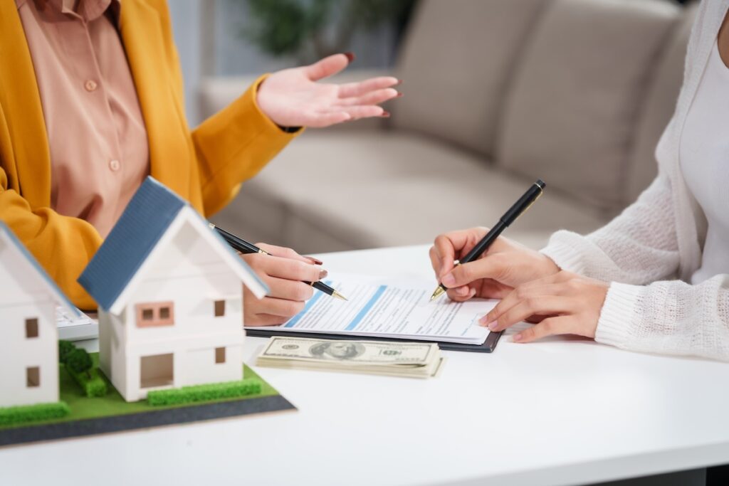 Asian businesswoman discusses home purchase contracts with clients at her desk, focusing on loans, mortgages, and other financial aspects of real estate transactions.