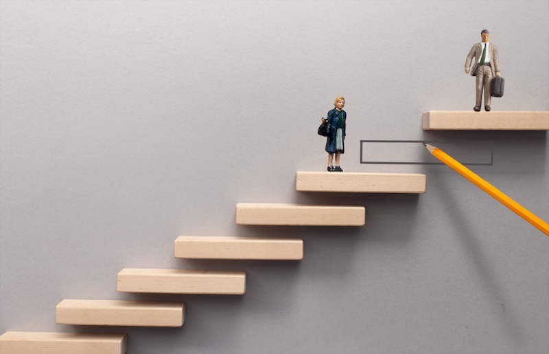 Miniature woman and man standing on wooden steps on different levels with pencil drawing a step to bridge the gap