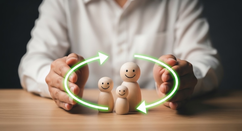 Hands protecting wooden family figures with a circular arrow, symbolizing protection and continuity