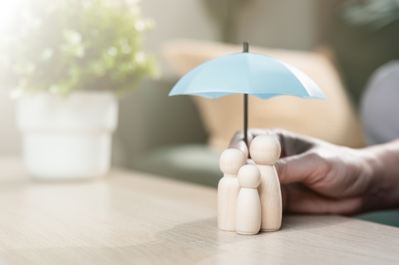 Life insurance and family protection concept with wooden figures under umbrella, representing financial security, insurance coverage, dependents protection, future planning, and long-term stability.