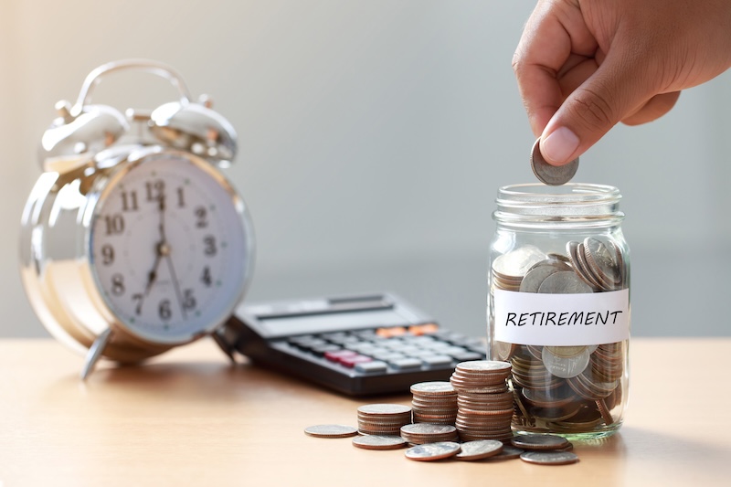 Hand putting Coins in glass jar with calculator and alarm clock for time to money saving for retirement concept ,  retirement planning.