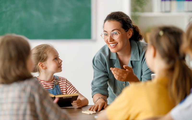 Happy kids and teacher at school. Woman and children are talking in the class.