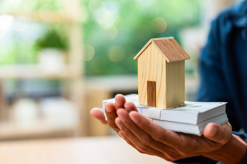 Real estate investment and property wealth concept featuring a wooden house model on cash savings, home ownership, mortgage financing, financial security, asset growth, and housing investment.