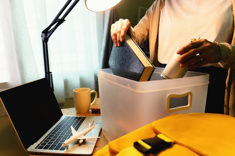 Female student abroad moving and keep the book in plastic box and backpack with laptop on desk at home to prepare for the journey to go back to study at university.