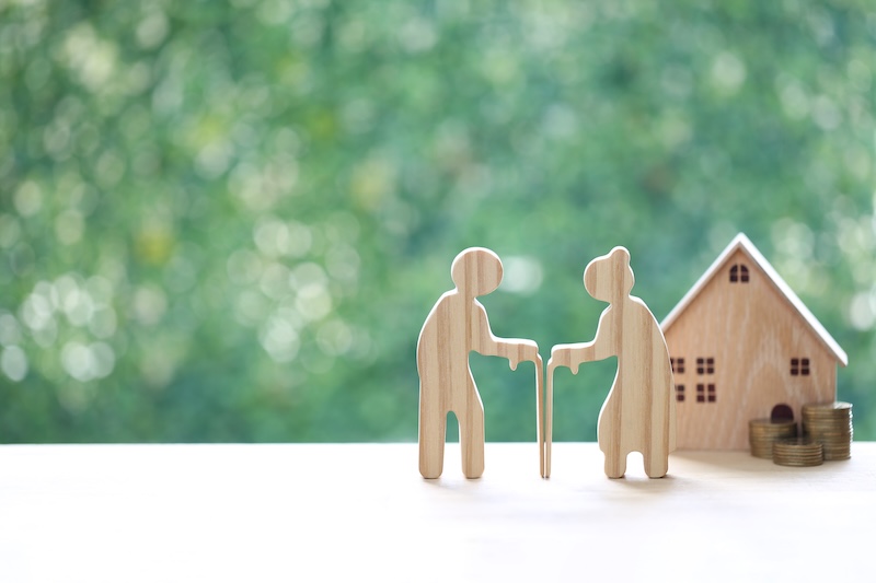Couple wooden figures standing with a miniature house and coins, representing retirement home planning, property investment, real estate for seniors and financial security for old age.